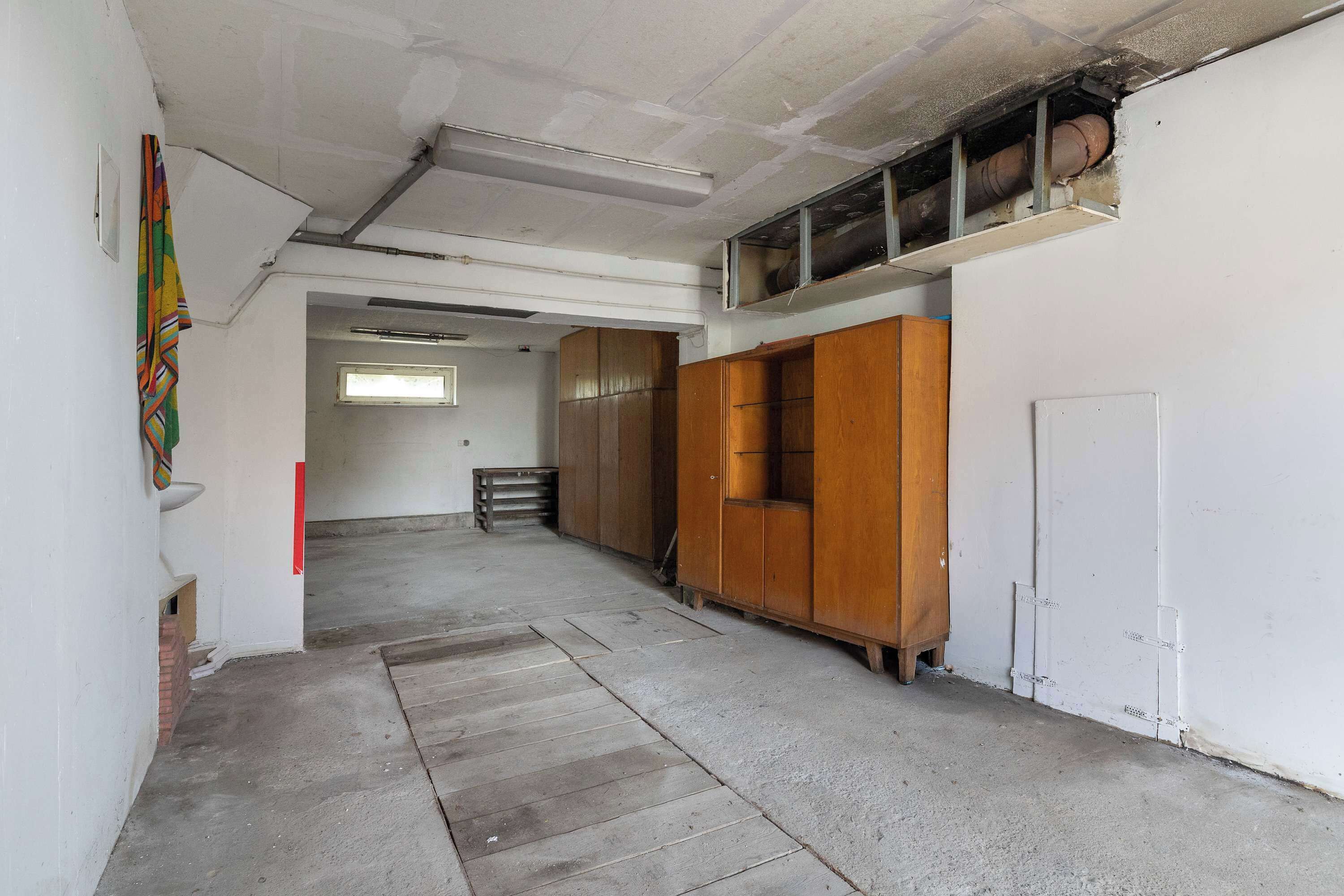 Ein schmaler Flur mit einem Holzschrank, einer weißen Tür und einem Fenster am Ende.