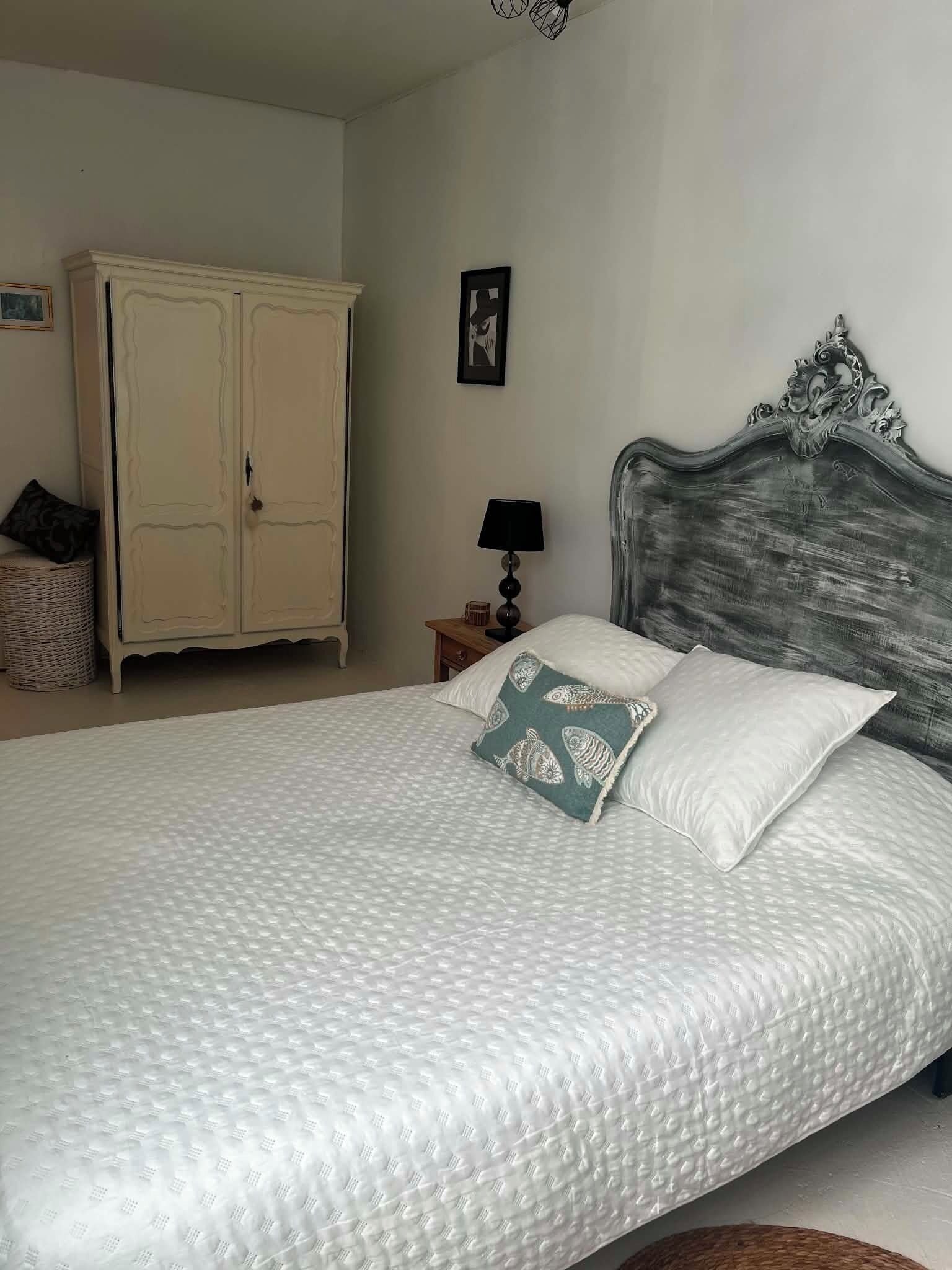 A bedroom with a bed, a wardrobe, a nightstand, and a lamp.