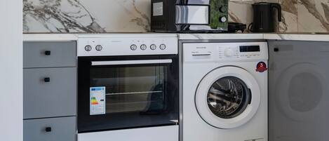A compact kitchen with a built-in oven, microwave, and washing machine.