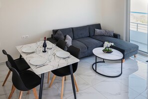A modern living space with a dining area, a grey sofa, and a small round table with a plant. - Kamiros Seaside Apartment in Kamiros Skala (Rhodes)