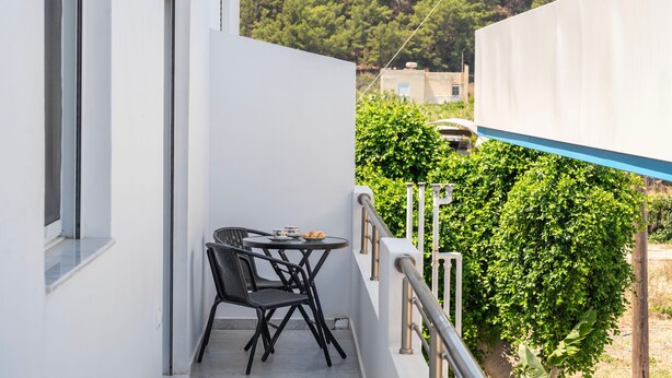 Ein Balkon mit Tisch und Stühlen, mit Blick auf eine üppige, grüne Landschaft mit Bäumen und einem Gebäude im Hintergrund.