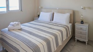 Ein ordentlich bezogenes Bett mit gestreifter Bettdecke, ein Nachttisch mit Lampe und ein Fenster mit Jalousien.