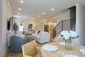 Ein modernes Wohnzimmer mit Sofa, Esstisch mit Stühlen, Küchenzeile und einer Treppe.