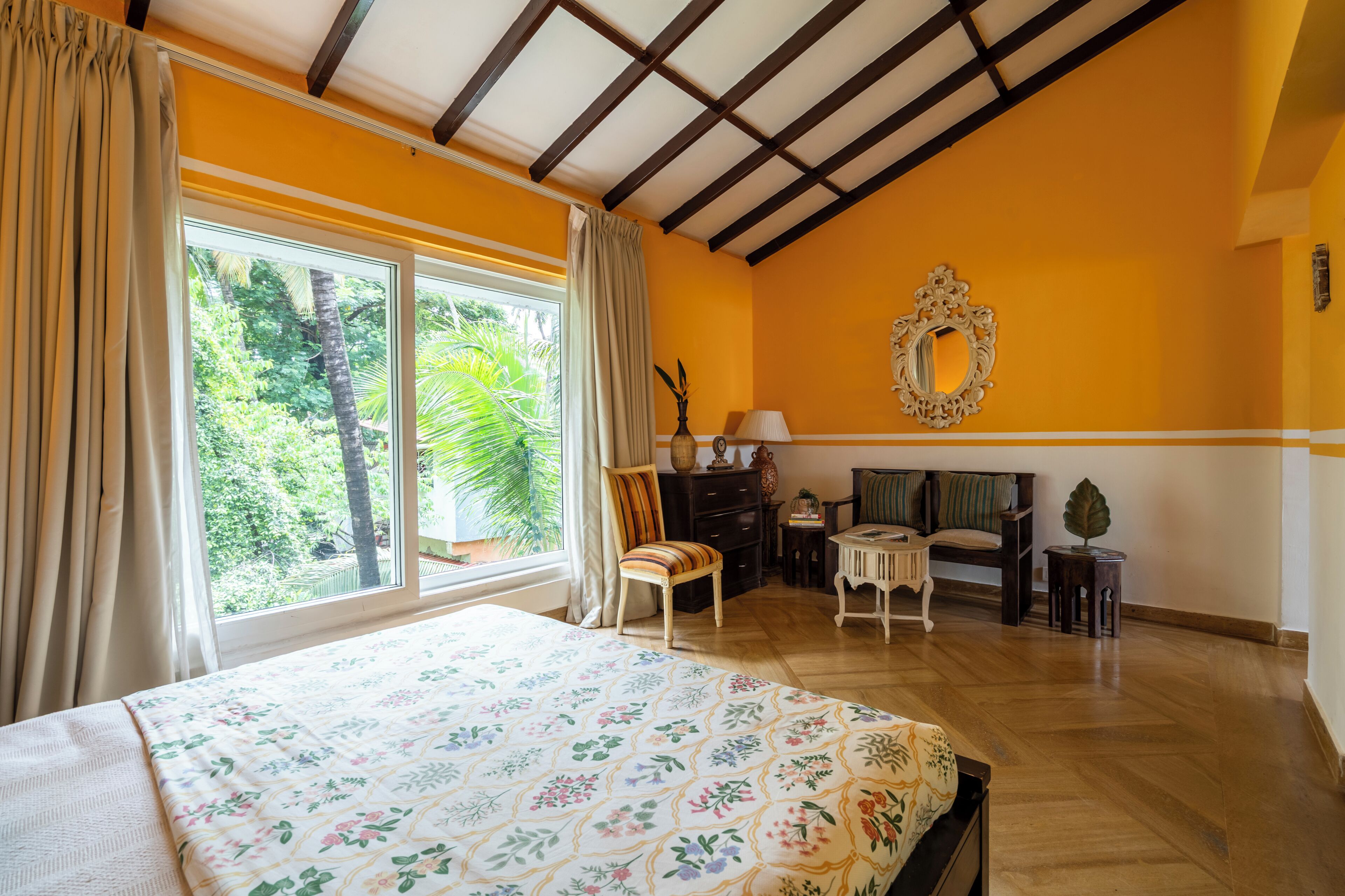 Un dormitorio con una cama grande, una silla, un sofá, una mesita y un espejo en la pared.