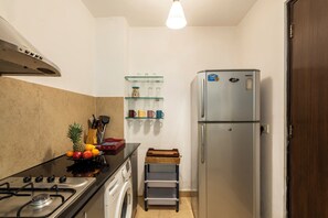 Cuina compacta amb fogó de gas, rentadora, nevera i una estant amb recipients de cuina.