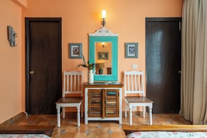 A room with two white chairs, a wooden cabinet, a mirror with a teal frame, and a wall-mounted light fixture. - Staymaster Divli - 3BR Villa in Candolim (Candolim)