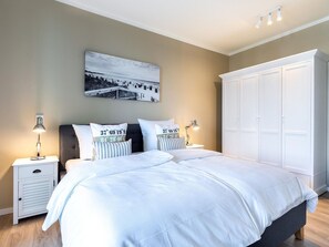 A bedroom with a bed, two bedside tables, a nightstand, a white wardrobe, and a wall-mounted picture. - Gemutliche Ostsee-oase, 4 Gaste (Lübeck)