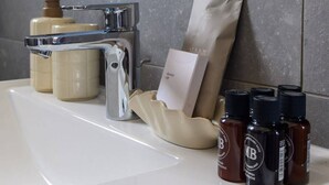 Een badkamer met een witte wastafel, een zeepdispenser, een douchemuts en een verzorgingsset.