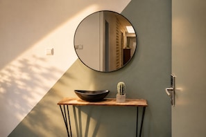 Ein modernes Badezimmer mit rundem Spiegel, Waschtisch aus Holz, einer schwarzen Schüssel und einer Kakteenpflanze.
