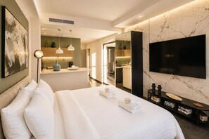 Et moderne hotelværelse med en stor seng, fjernsyn, minibar og et badeværelse, der kan ses gennem en åben dør.