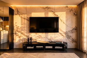 A modern living room with a large flat-screen TV mounted on a marble wall, a black entertainment unit with books, and a minimalist design. - Athens Majesty Supreme Suite - Located in the heart of Athens (Athina)