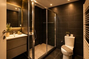Et moderne badeværelse med en glasafskærmet brusekabine, toilet og håndvask med toiletartikler.
