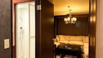 A hotel room with a shower, a sofa, a coffee table, and a chandelier.