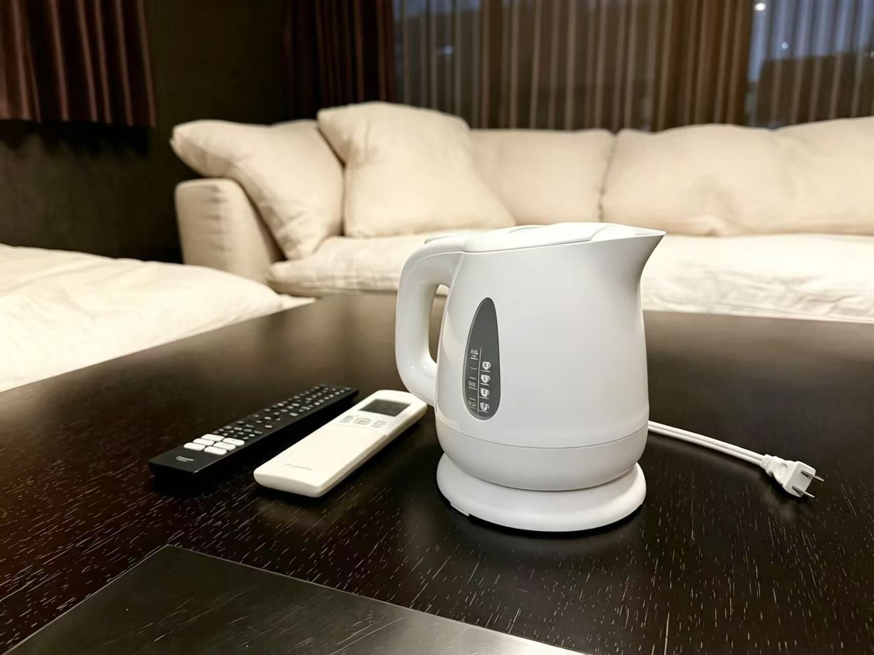 A white electric kettle on a dark wooden table with a remote control beside it.