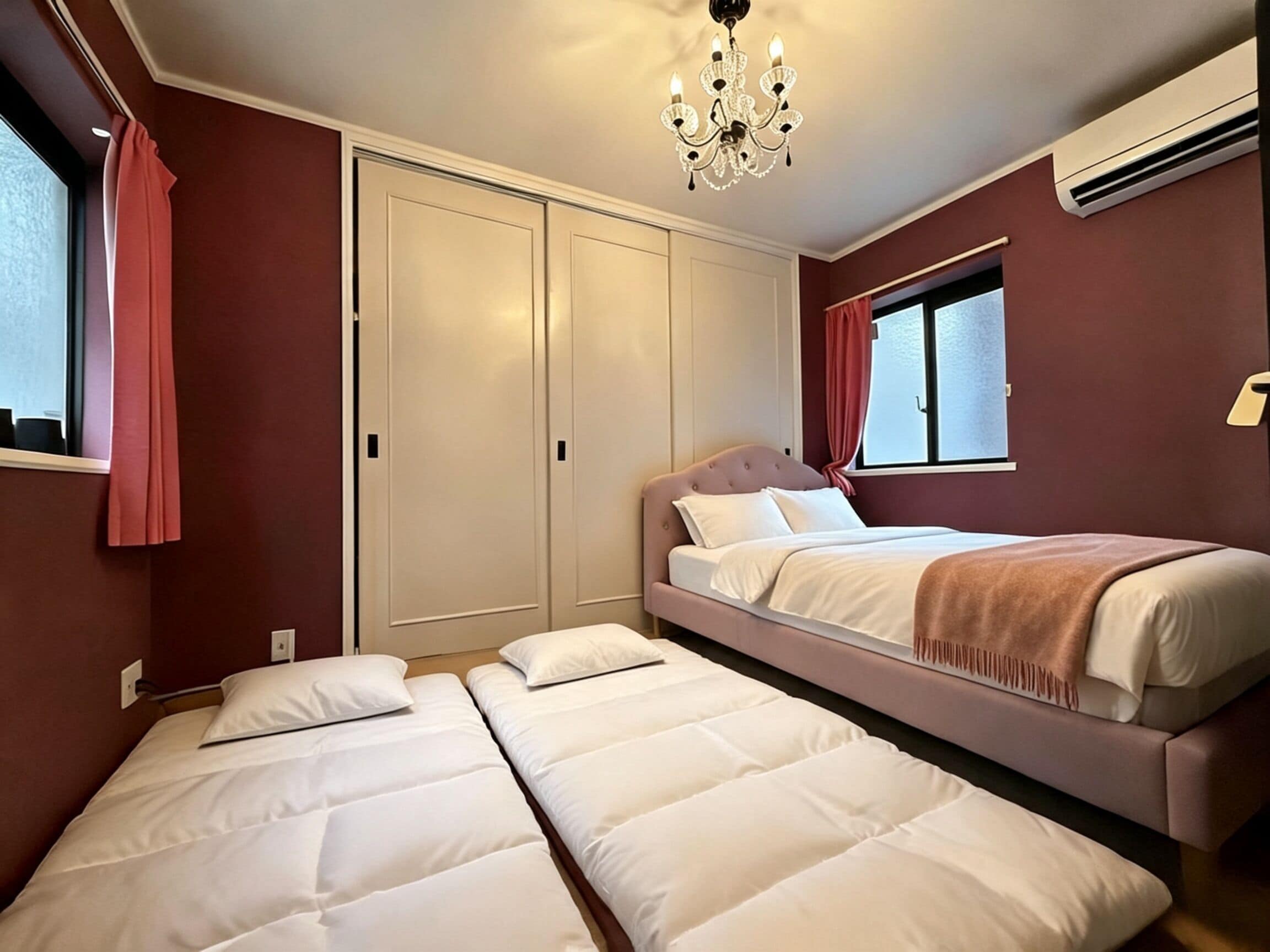 A hotel room with a double bed, a single bed, a wardrobe, and a window with curtains.