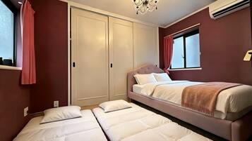 A hotel room with a double bed, a single bed, a wardrobe, and a window with curtains.