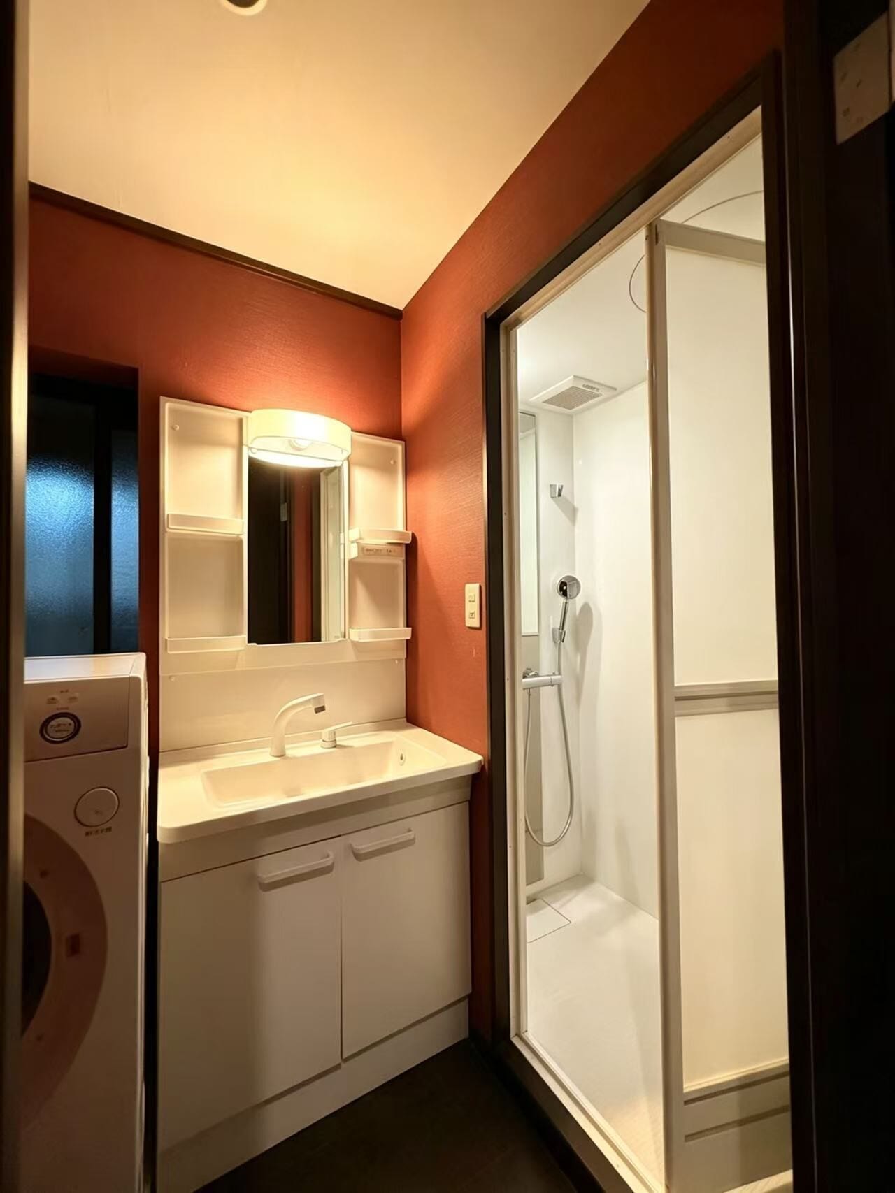 A compact bathroom with a white sink, mirror, and a glass-enclosed shower.