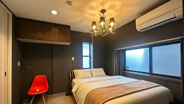 A bedroom with a bed, a red chair, a chandelier, and an air conditioning unit. - PIKA STAY Shimada House (Tokyo)