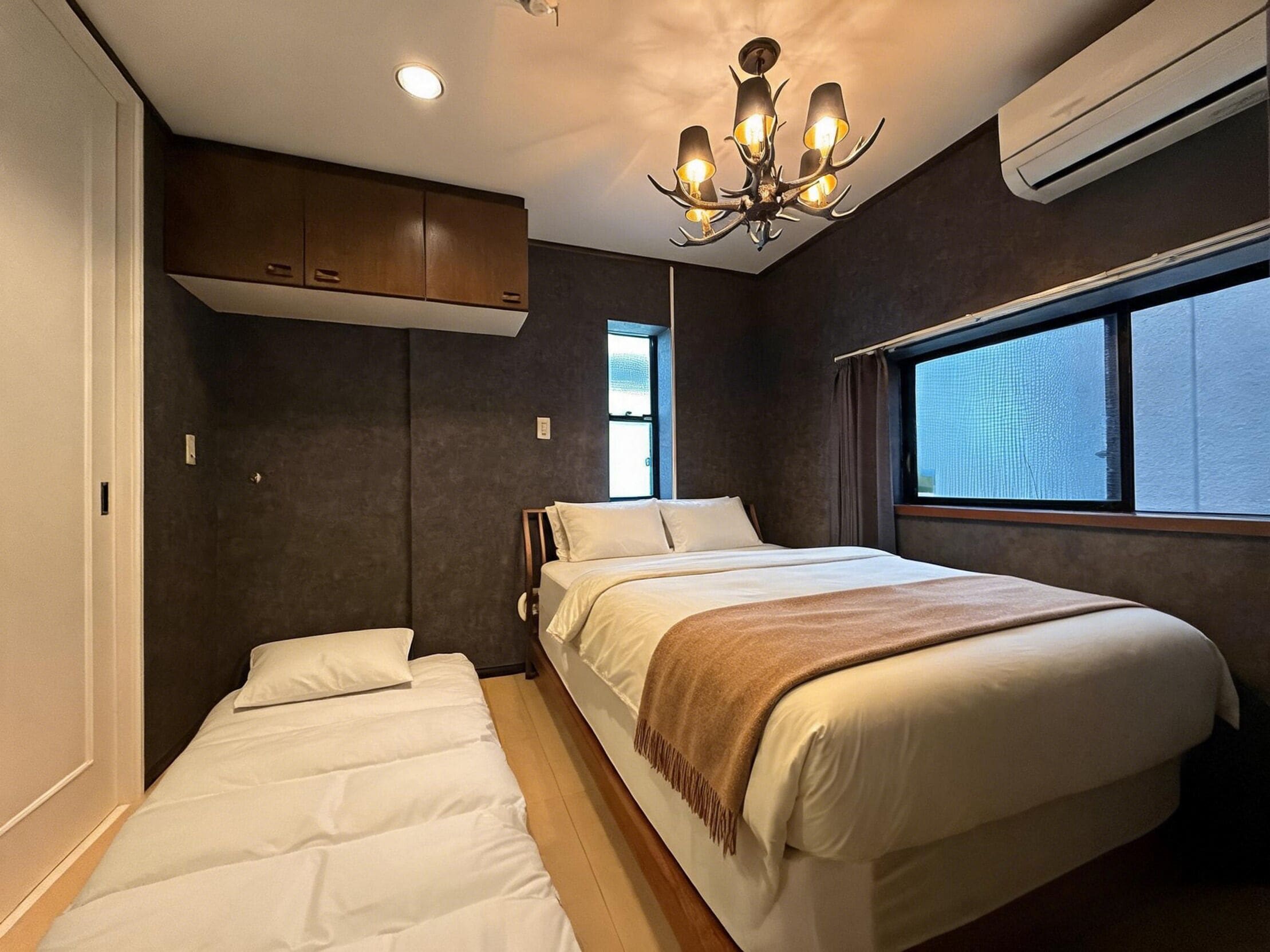 A bedroom with a bed, a window, a chandelier, and an air conditioning unit.