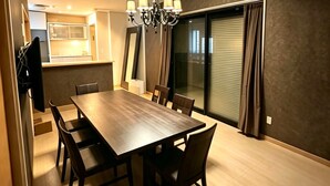 A dining area with a rectangular table and chairs, a chandelier, and a sliding glass door leading to a balcony. - PIKA STAY Shimada House (Tokyo)