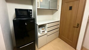 A compact kitchenette with a microwave, a small refrigerator, a bread maker, and a wooden door. - PIKA STAY Shimada House (Tokyo)