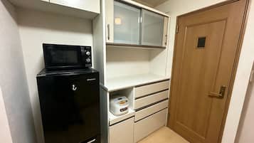A compact kitchenette with a microwave, a small refrigerator, a bread maker, and a wooden door.