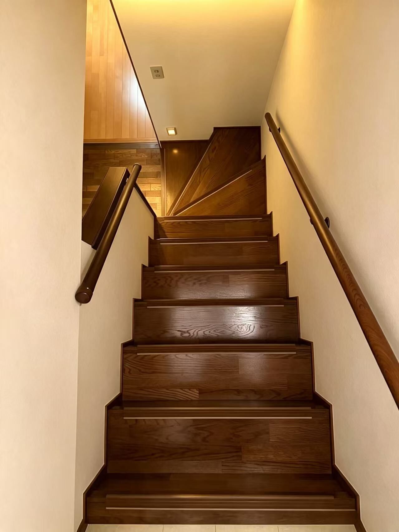 A wooden staircase with a handrail on the right and a wooden wall on the left.
