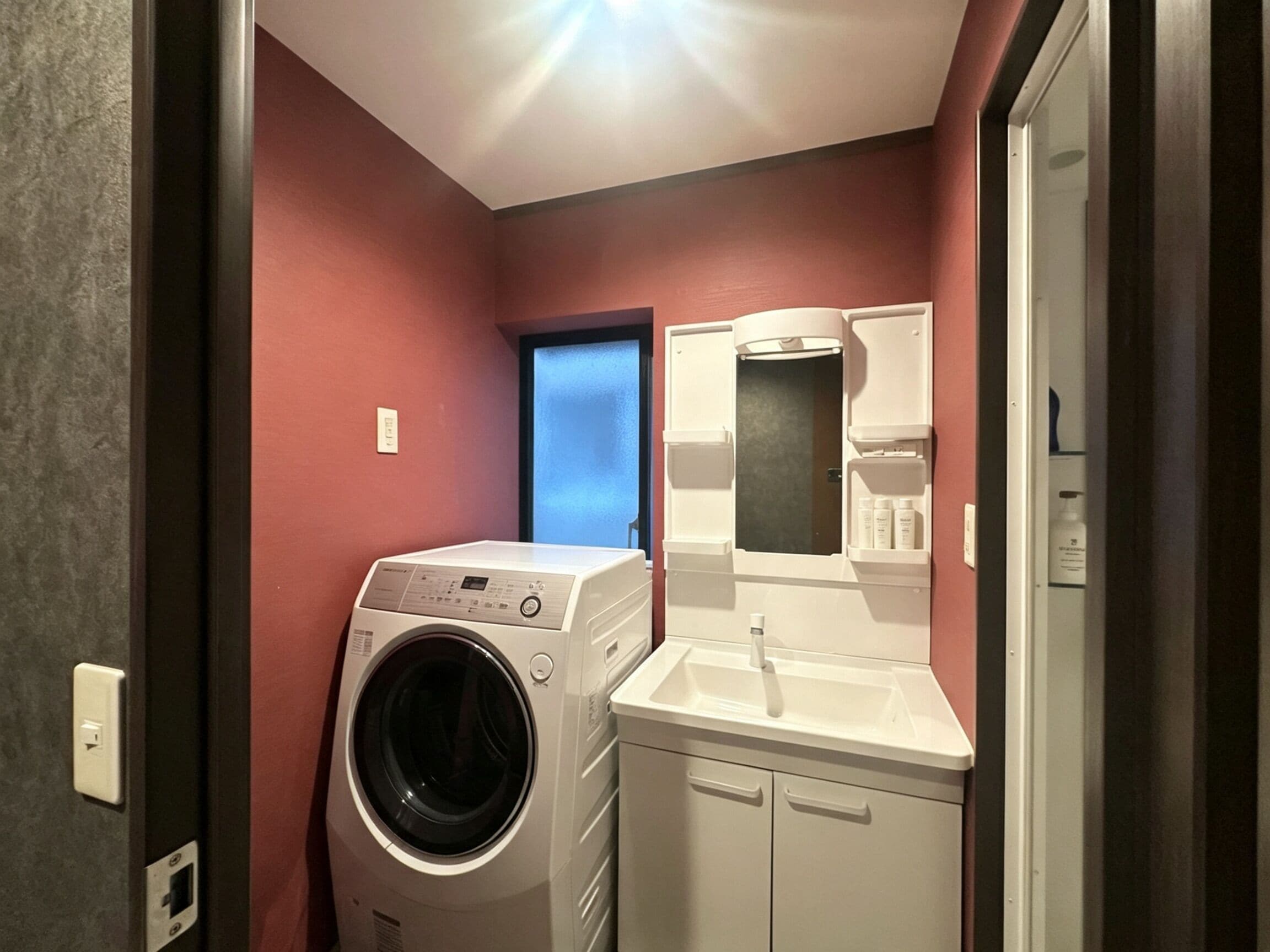 A compact laundry room with a washing machine, a sink, and a mirror.