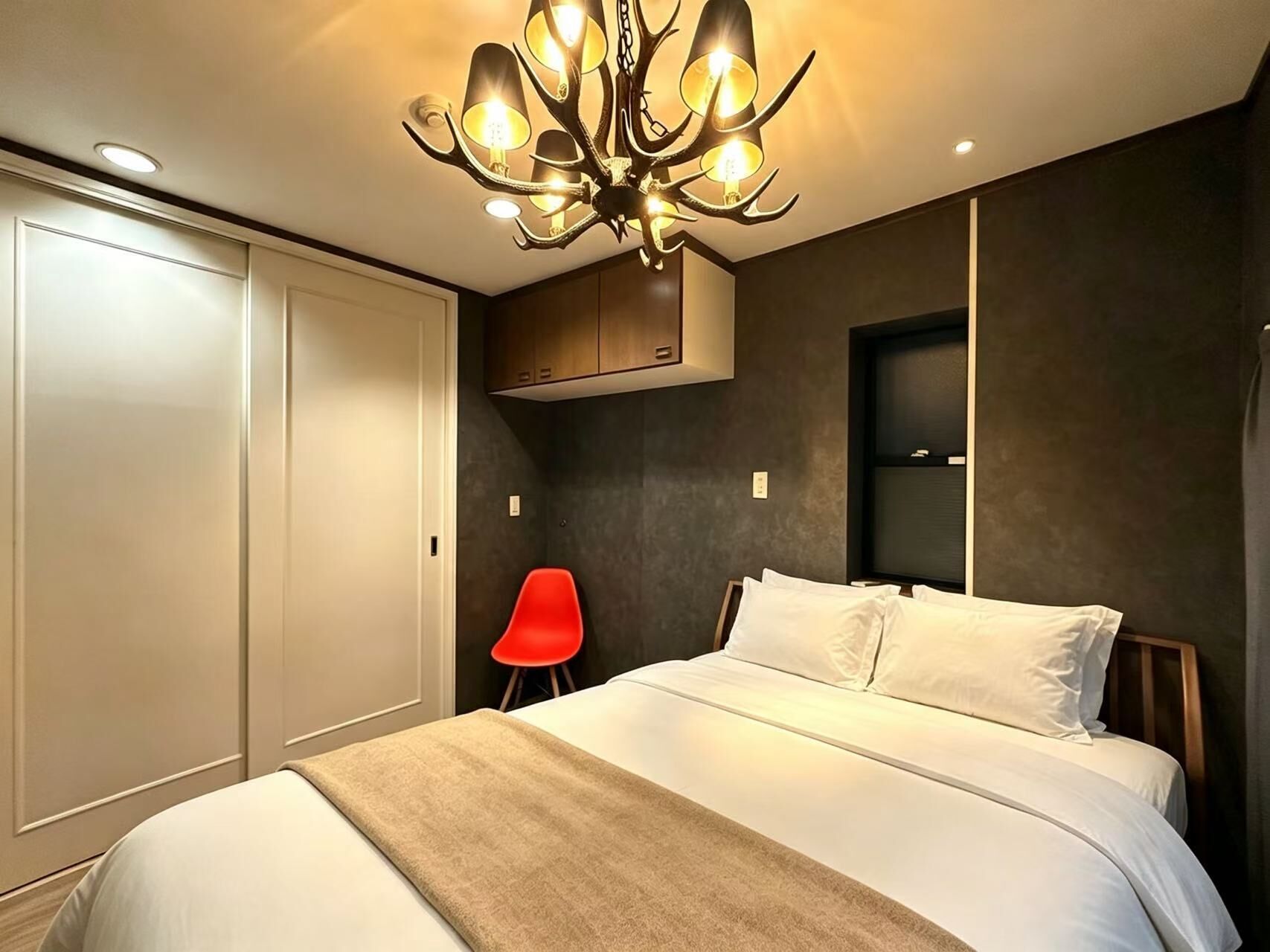 A bedroom with a large bed, a red chair, a wardrobe, and a chandelier.