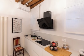 A kitchen with white cabinets, a black range hood, a wooden chair, a kettle, and a coffee maker on the counter. - Ea casa de mì2 – The Enchantment of Living Venice (Venezia)