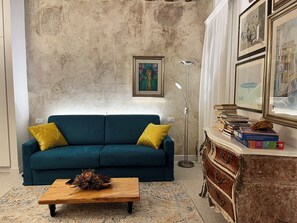 A living room with a teal sofa, a wooden coffee table, a patterned rug, a floor lamp, and a bookshelf with books. - Ea casa de mì2 – The Enchantment of Living Venice (Venezia)