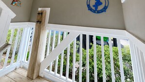 Um quarto com um corrimão branco, uma luminária no teto e várias decorações nas paredes, incluindo uma placa com a inscrição 'TO THE BEACH' e uma fotografia emoldurada.