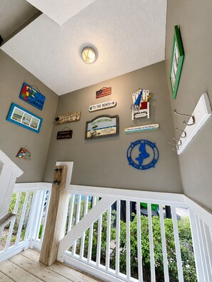 A room with a white railing, a ceiling light, and various wall decorations including a sign that says 'TO THE BEACH' and a framed picture. - Lady Luck - Second Row in Surfside Beach (Surfside Beach)