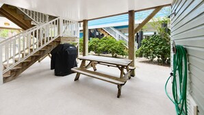 Uma área externa coberta com um banco de madeira, churrasqueira e escada para um andar superior.