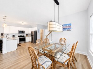 A modern kitchen with white cabinets, stainless steel appliances, and a dining area with a glass table and wicker chairs. - Lady Luck - Second Row in Surfside Beach (Surfside Beach)