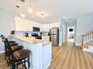 A modern kitchen with white cabinets, stainless steel appliances, and a marble island with bar stools. - Lady Luck - Second Row in Surfside Beach (Surfside Beach)