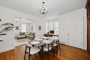 Ein moderner Essbereich mit einer Chandelier, einem Esstisch mit Stühlen, einer Couch und einem Fernseher im Hintergrund.