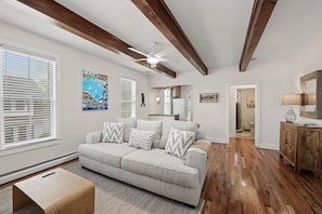 A living room with a sofa, a coffee table, a ceiling fan, and a kitchen area visible through an open door. - Escape to this spacious three-level home in the heart of Ocean Grove, just a short walk from the beach, boardwalk, shops, and restaurants. (Neptune Township)