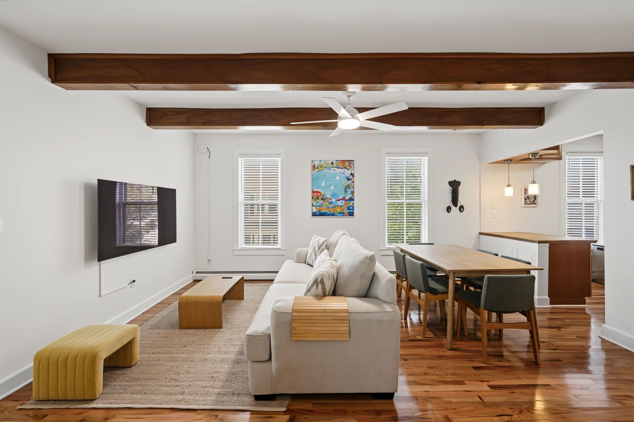 A modern living room with a sofa, a dining table with chairs, a ceiling fan, and artwork on the walls.