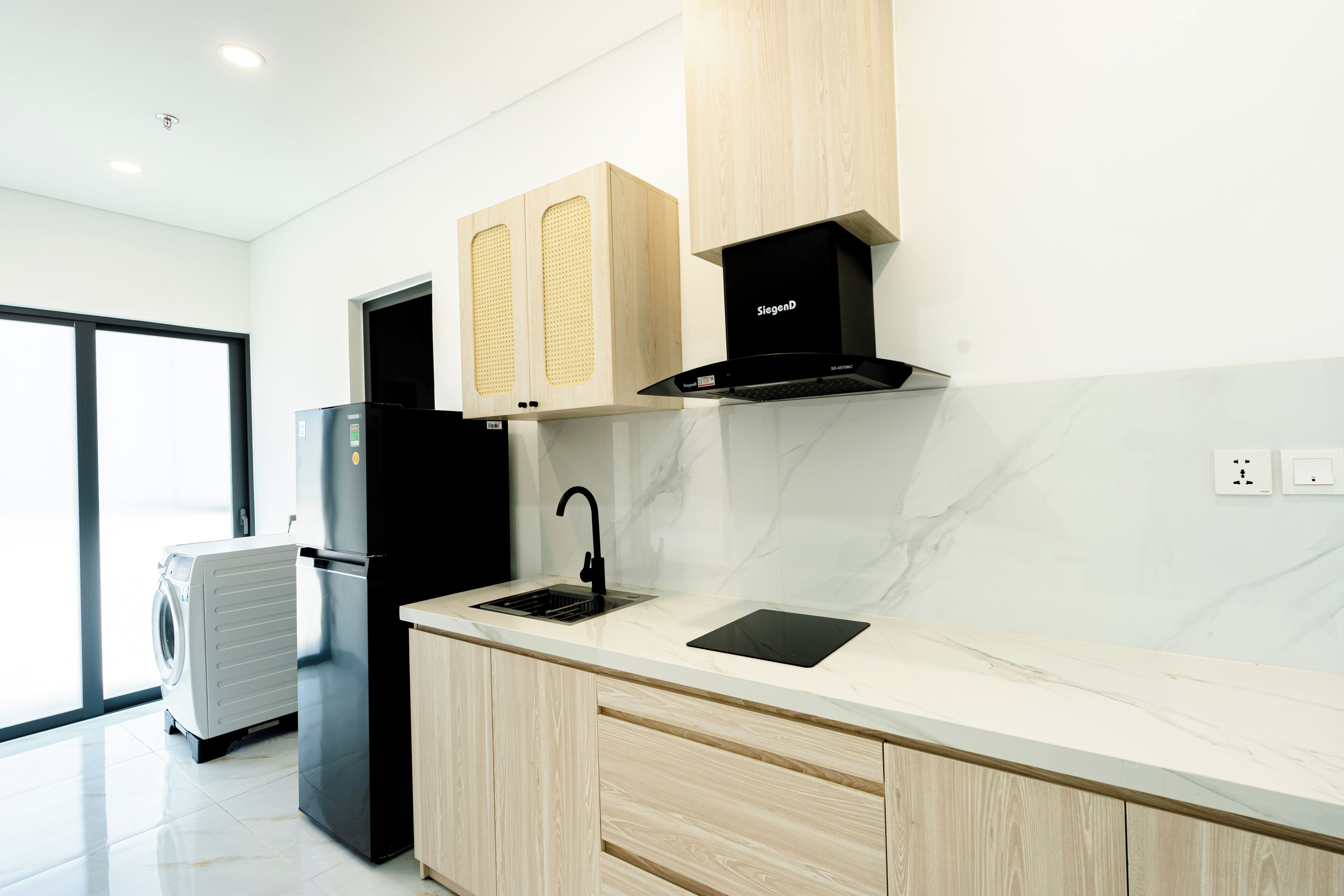 A modern kitchen with a built-in dishwasher, a black refrigerator, wooden cabinets, a black range hood, and a marble countertop.