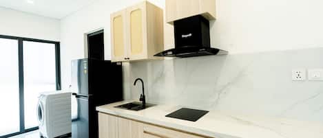 Una cocina moderna con lavavajillas integrado, un refrigerador negro, armarios de madera, una campana extractora negra y una encimera de mármol.