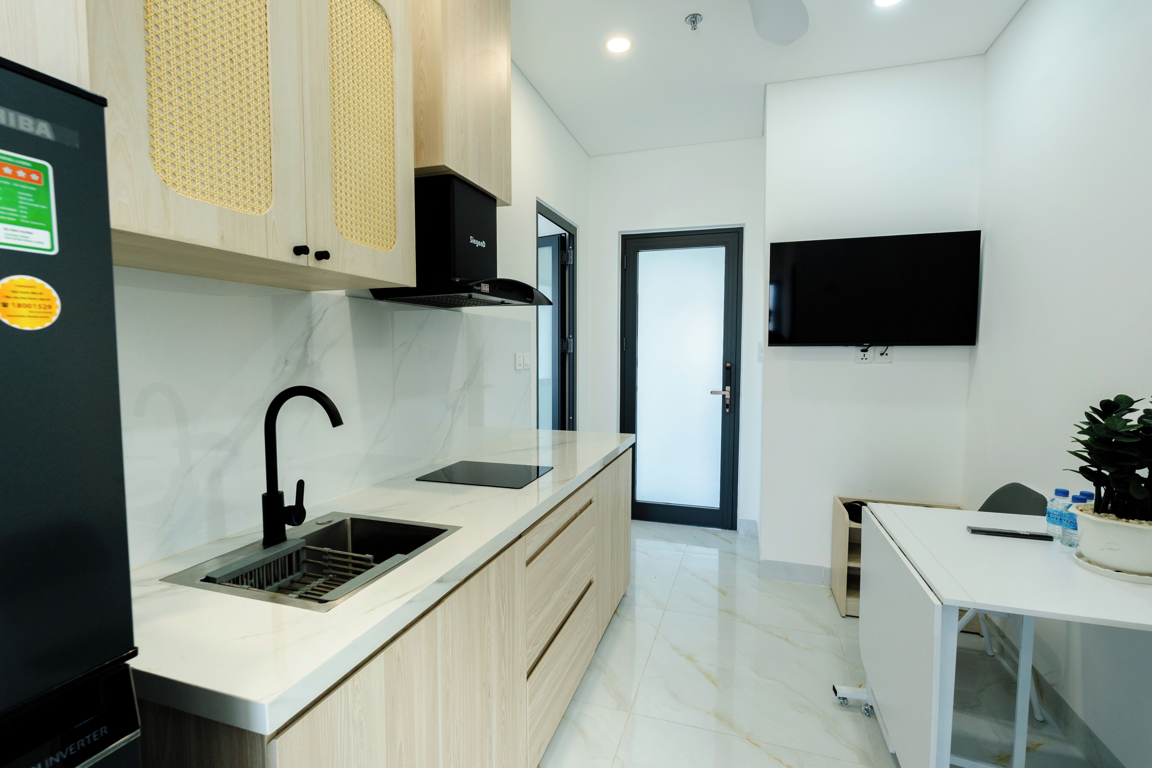 A modern kitchen with a built-in stove, sink, and a flat-screen TV mounted on the wall.