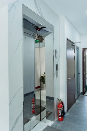Um elevador com mostrador digital, um extintor de incêndio e uma porta com fechadura.