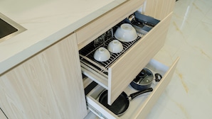 Una cocina con horno empotrado, microondas y un cajón con utensilios de cocina.