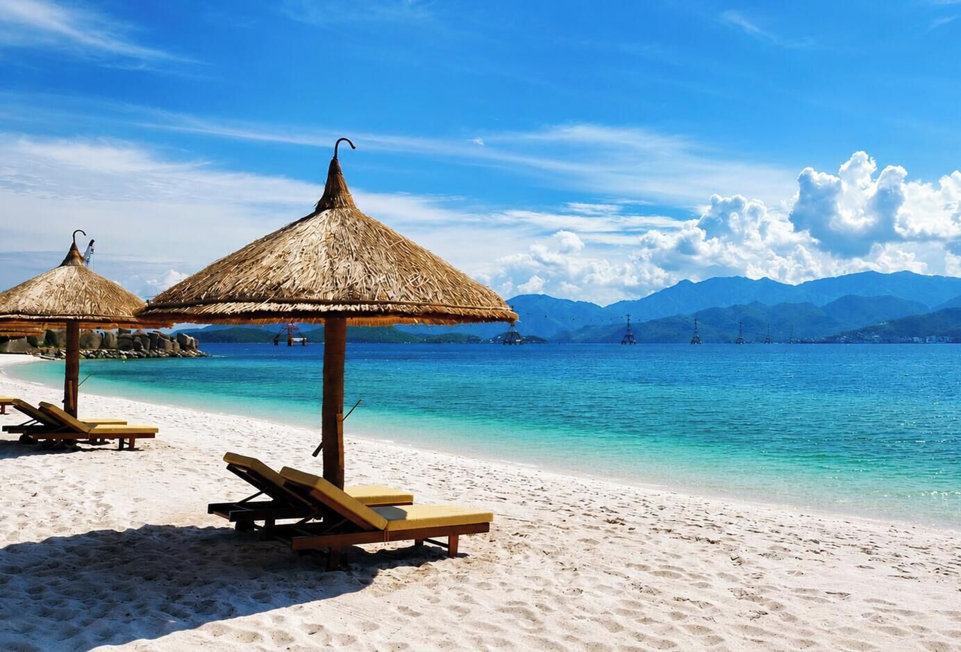 Una playa con sombrillas de paja y sillones de madera.