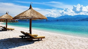 Una playa con sombrillas de paja y sillones de madera.