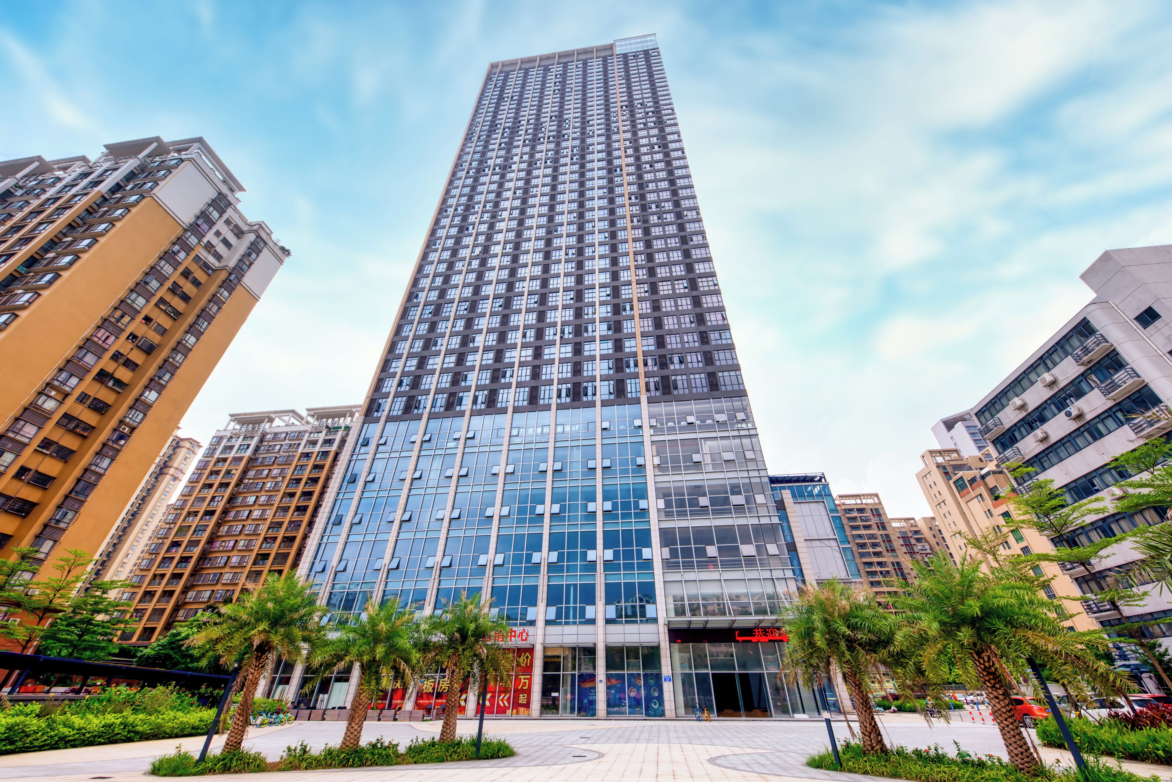 A high-rise building with a modern glass facade, surrounded by other high-rise buildings and palm trees.