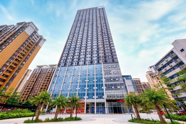 A high-rise building with a modern glass facade, surrounded by other high-rise buildings and palm trees.