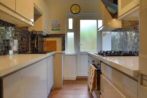 Una cocina moderna con armarios blancos, un salpicadero de azulejos negros, una estufa a gas y un reloj en la pared.