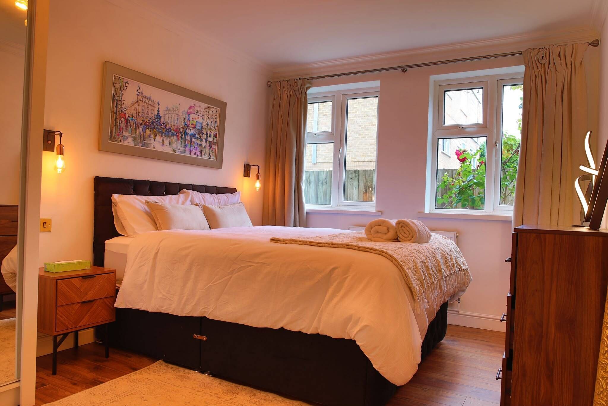 A bedroom with a bed, a nightstand, a dresser, a painting, and two windows.